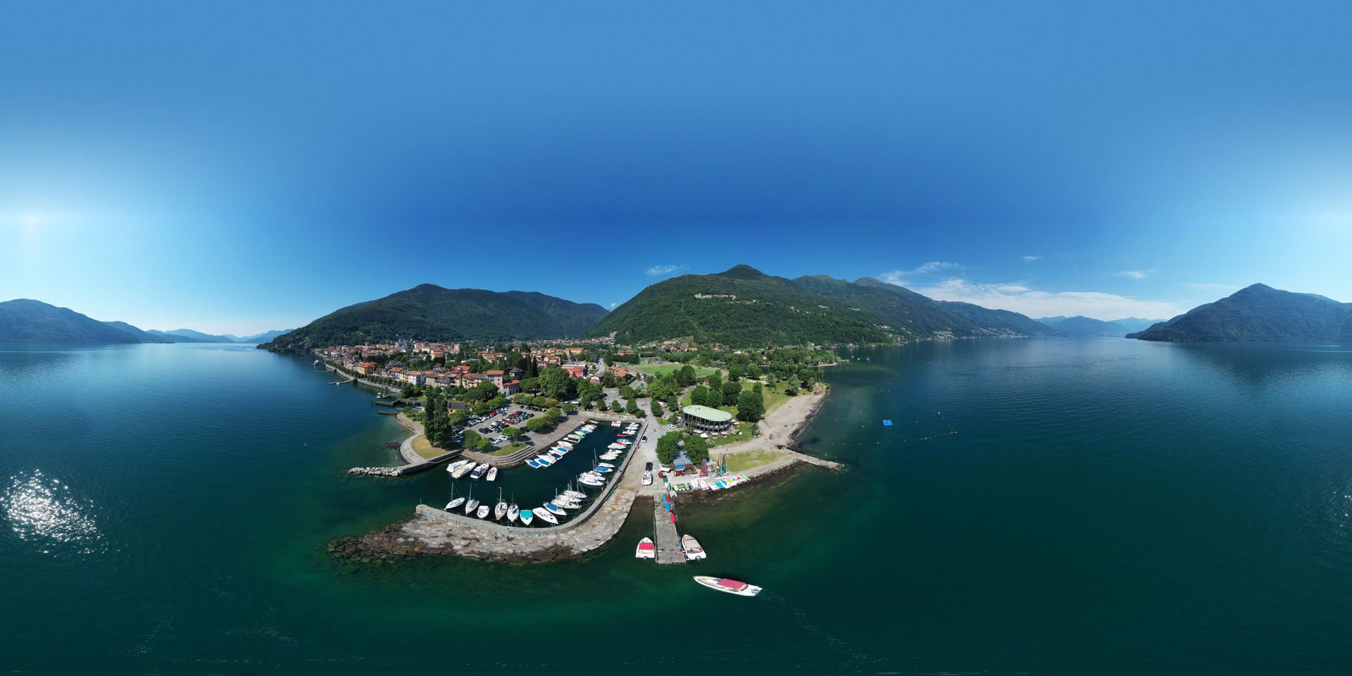 Aerial view of a coastal town with a marina, blue water, and green hills under a cloudy sky