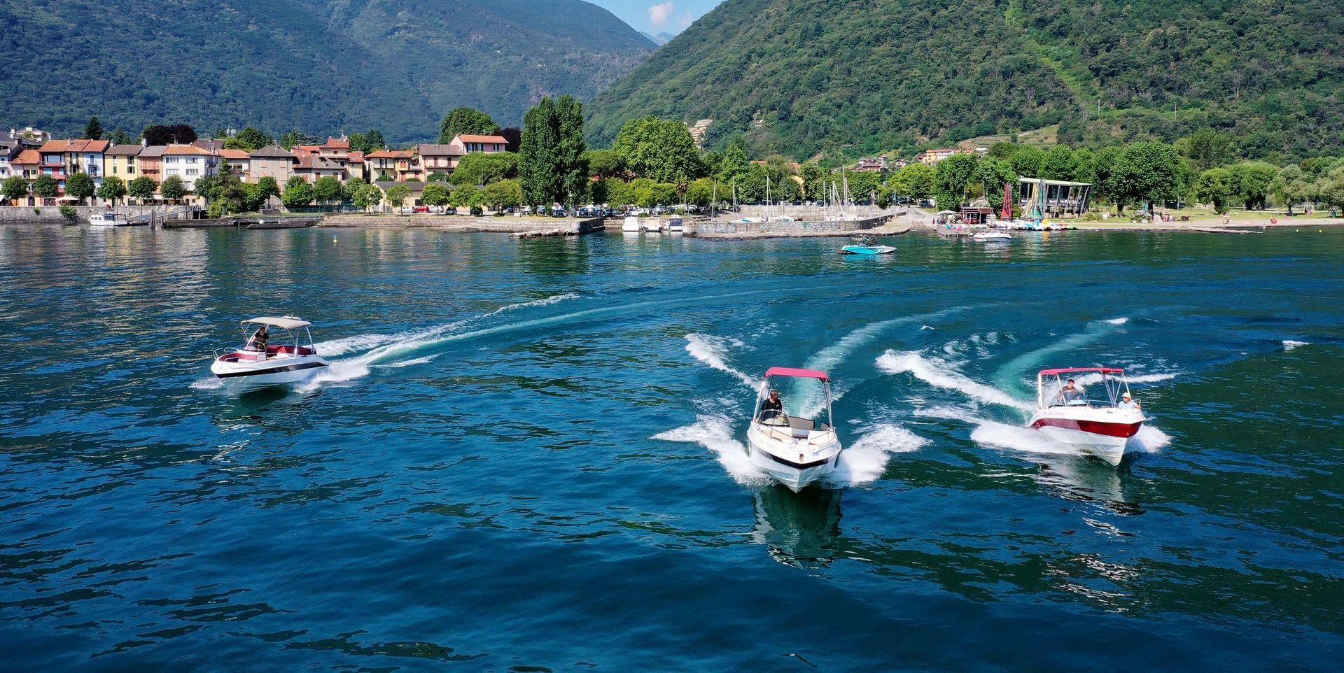 Speedboats racing across a blue lake with a mountain village in the background