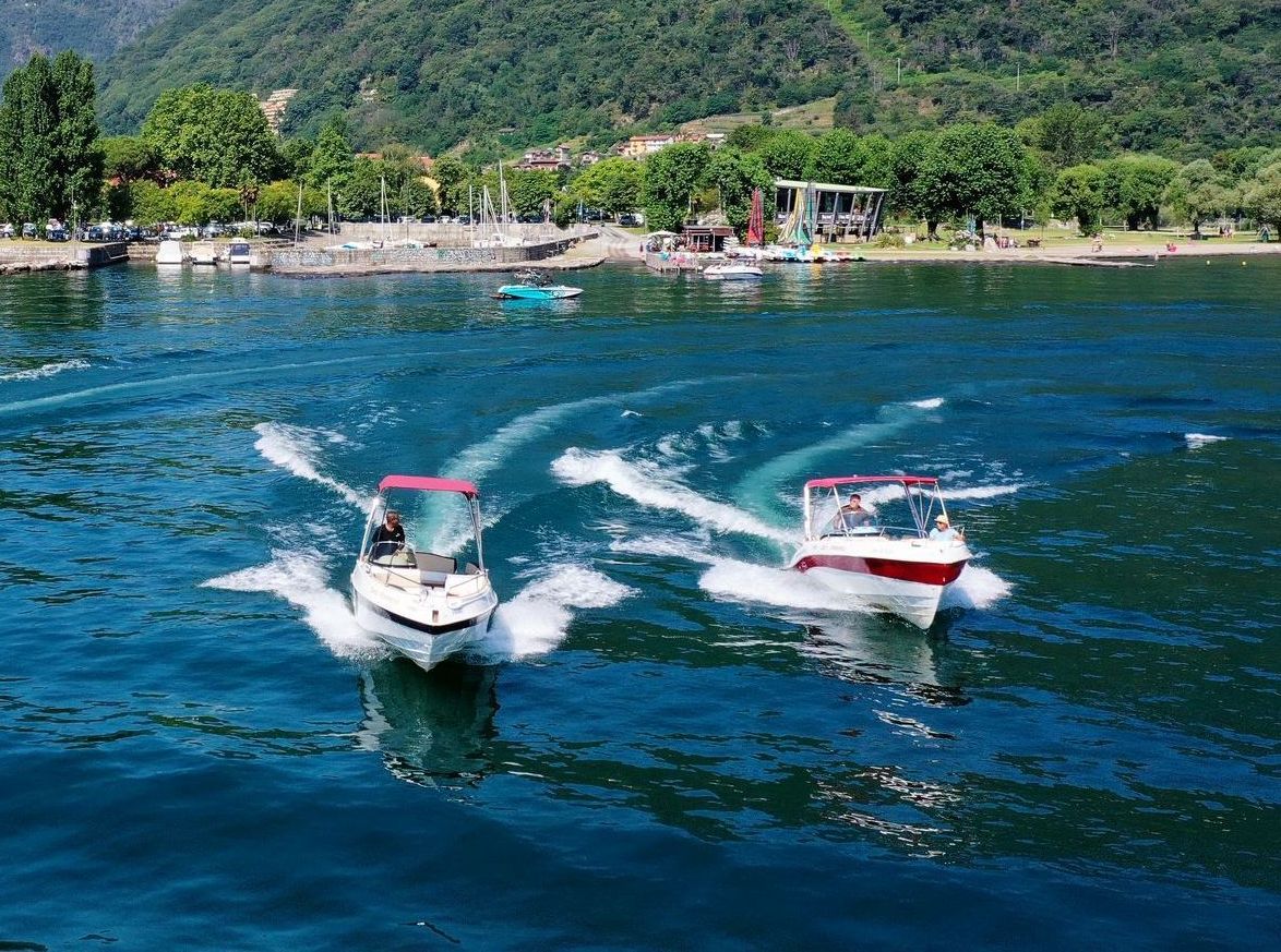 Two small motorboats speeding on blue water near a tropical shoreline with green hills.