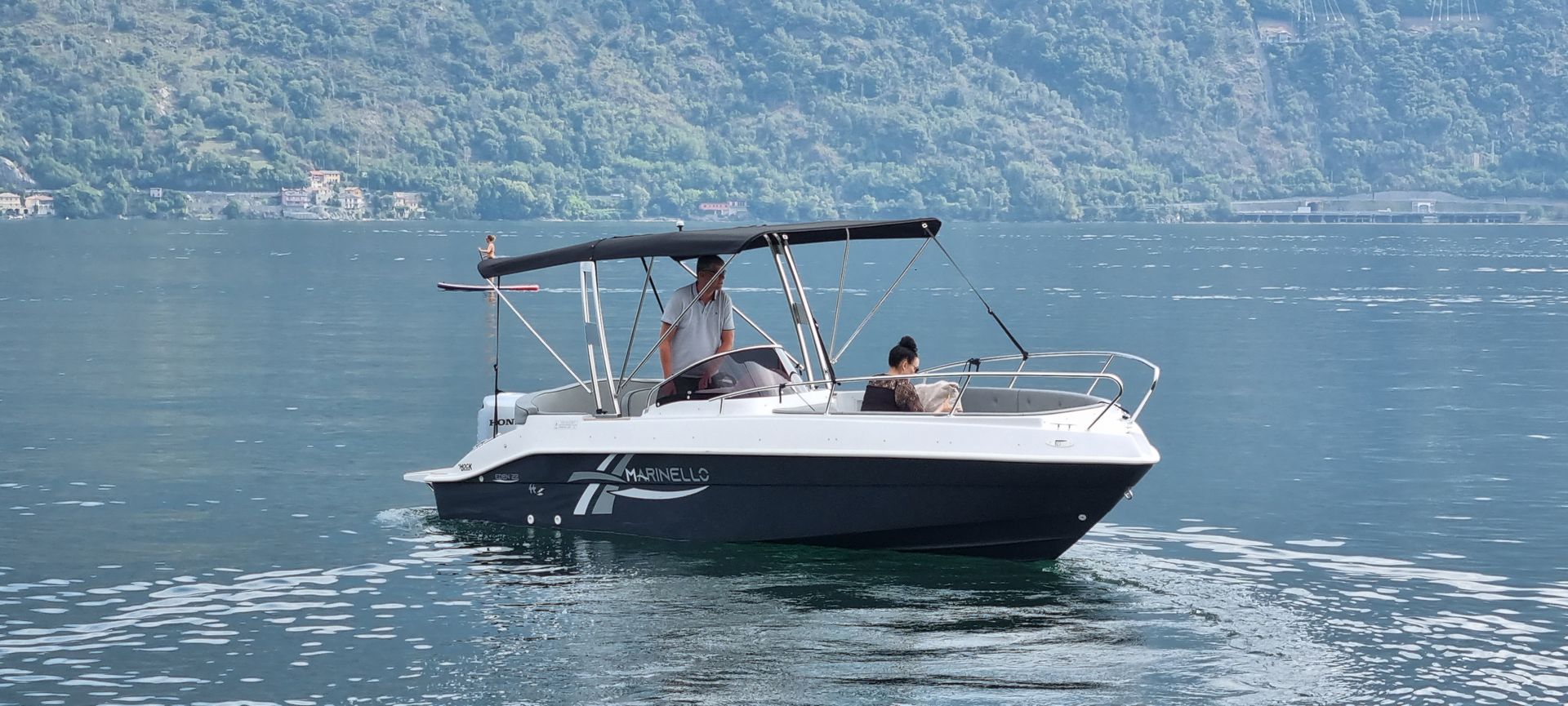 Small black-and-white motorboat with people on calm blue water near a mountain shore