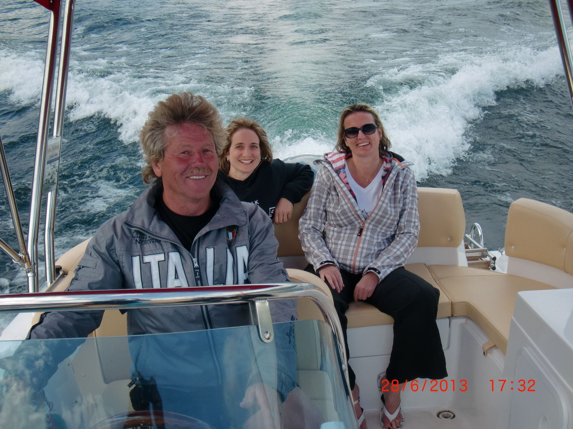 Three people smiling on a boat speeding across choppy water