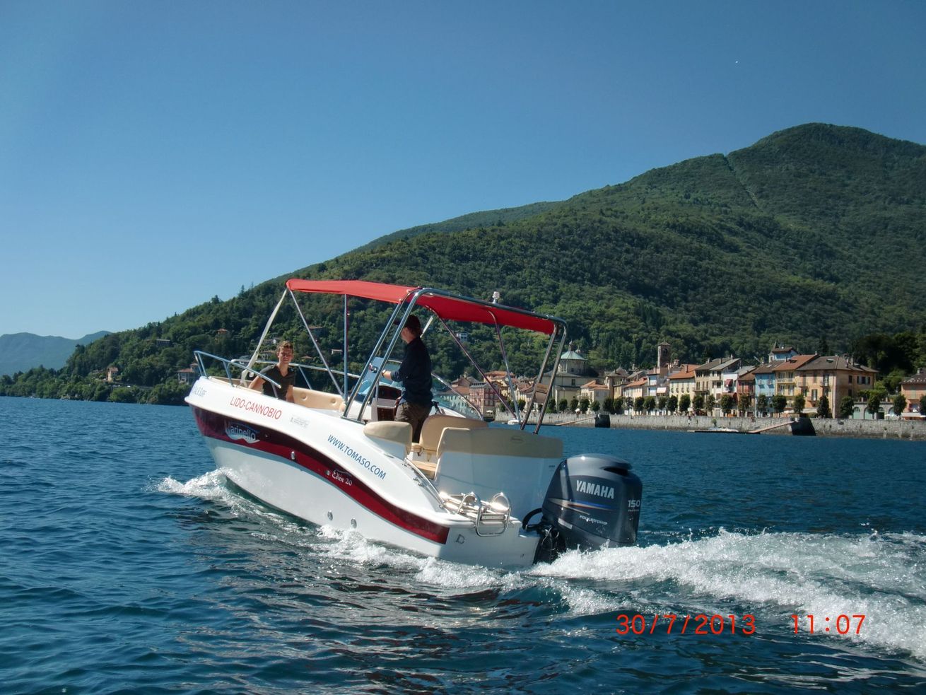 Small motorboat with red canopy on blue water near a green mountain shoreline