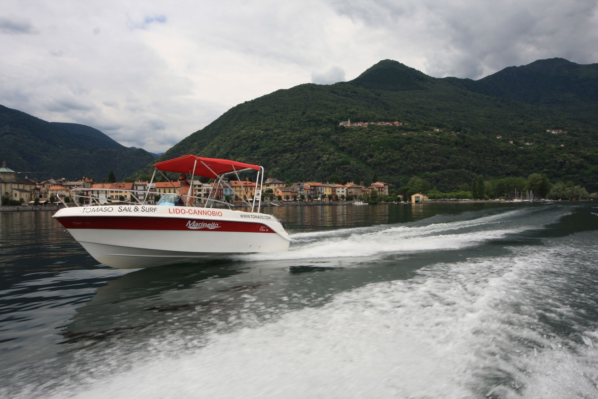 Red-and-white speedboat cruising across a lake with mountains and a lakeside town in the background