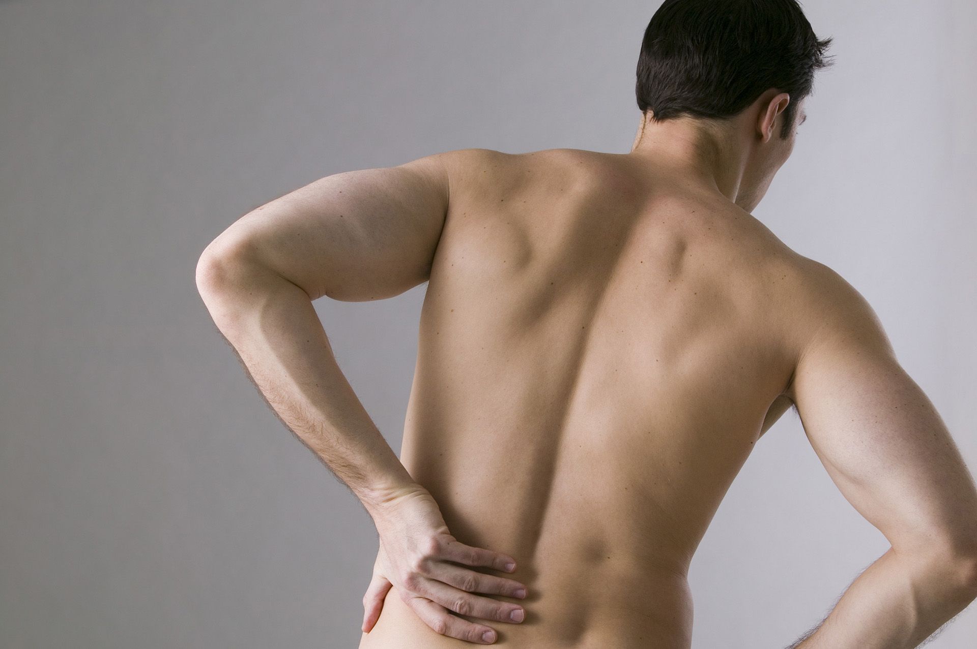 Un hombre sin camisa se sujeta la espalda con dolor.