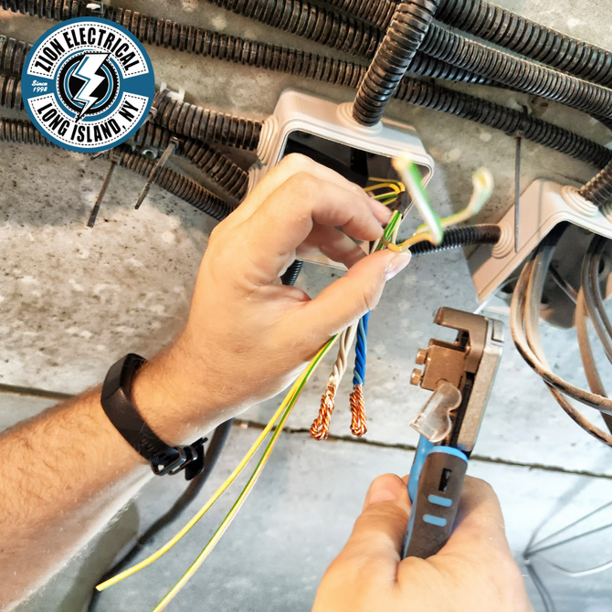 Person stripping wire with a tool near electrical boxes. Wires are yellow, green, blue, and brown. Setting is a wall.