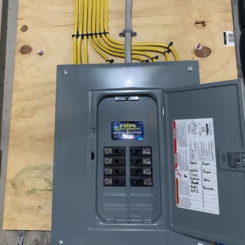 Electrical panel with open door, yellow wires, gray box, mounted on wood.
