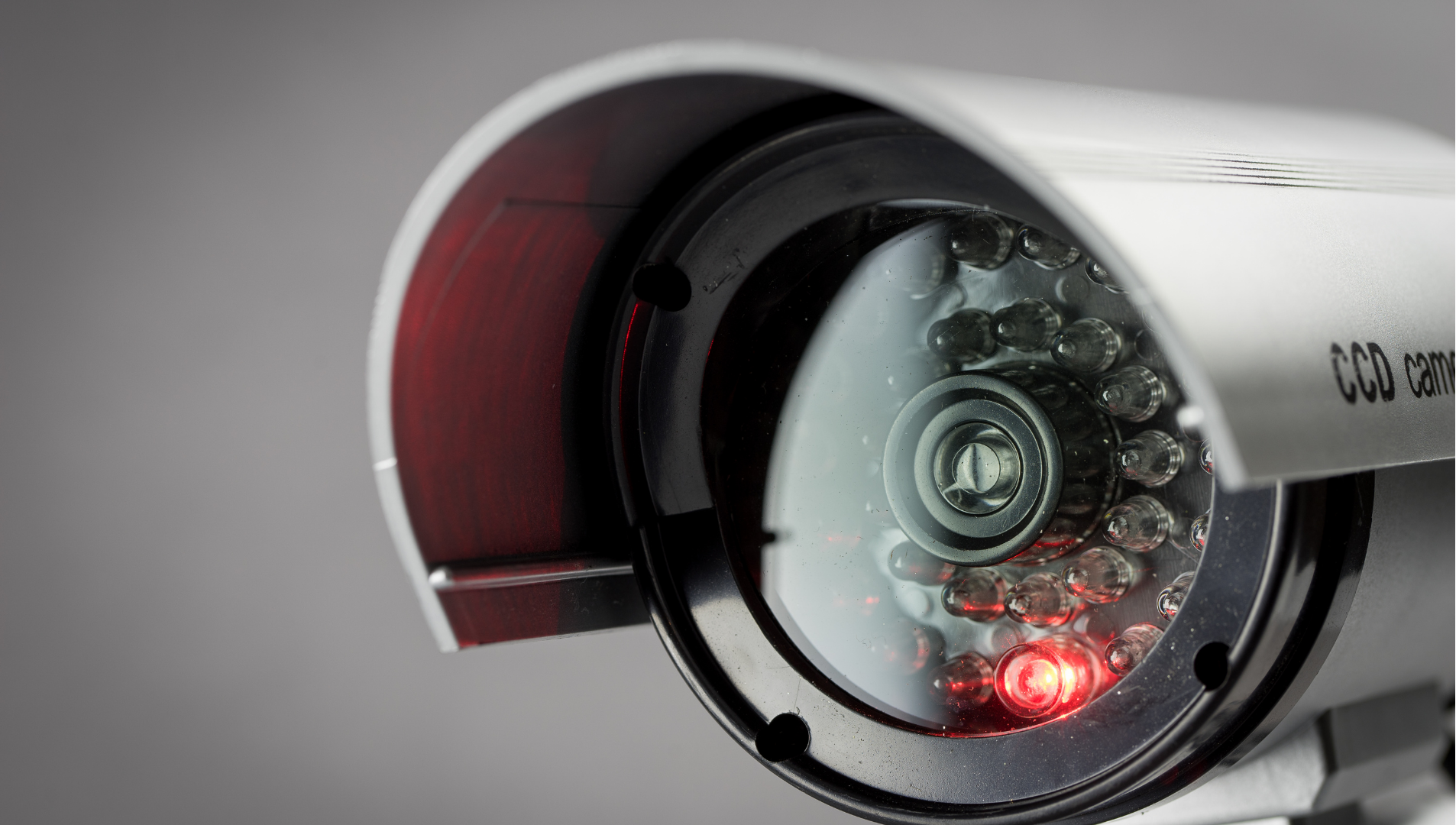 Close-up of a white CCTV security camera with glowing red infrared lights against a gray background
