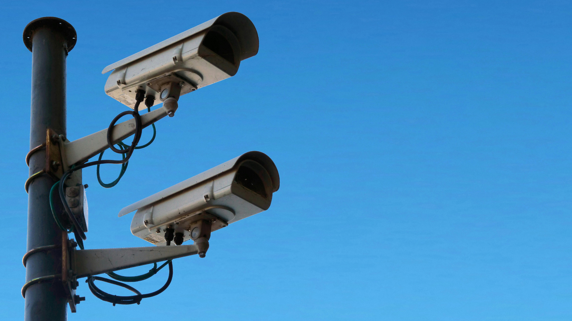 Two security cameras mounted on a pole against a clear blue sky