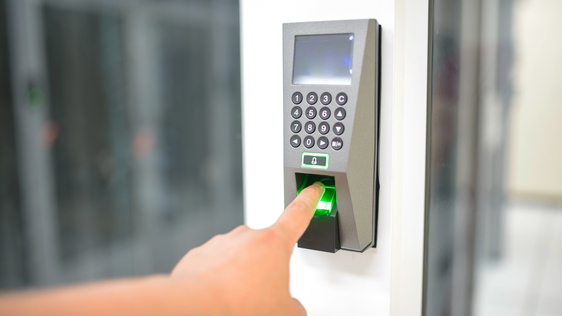 Finger pressing green-lit keypad on a door access control panel indoors