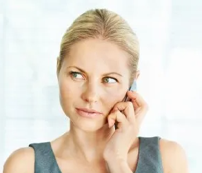 A person holding a mobile phone to their ear, looking to the side with a neutral expression.
