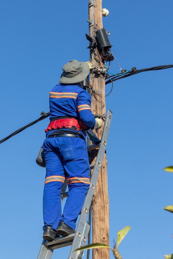 A man is standing on a ladder working on a power pole.