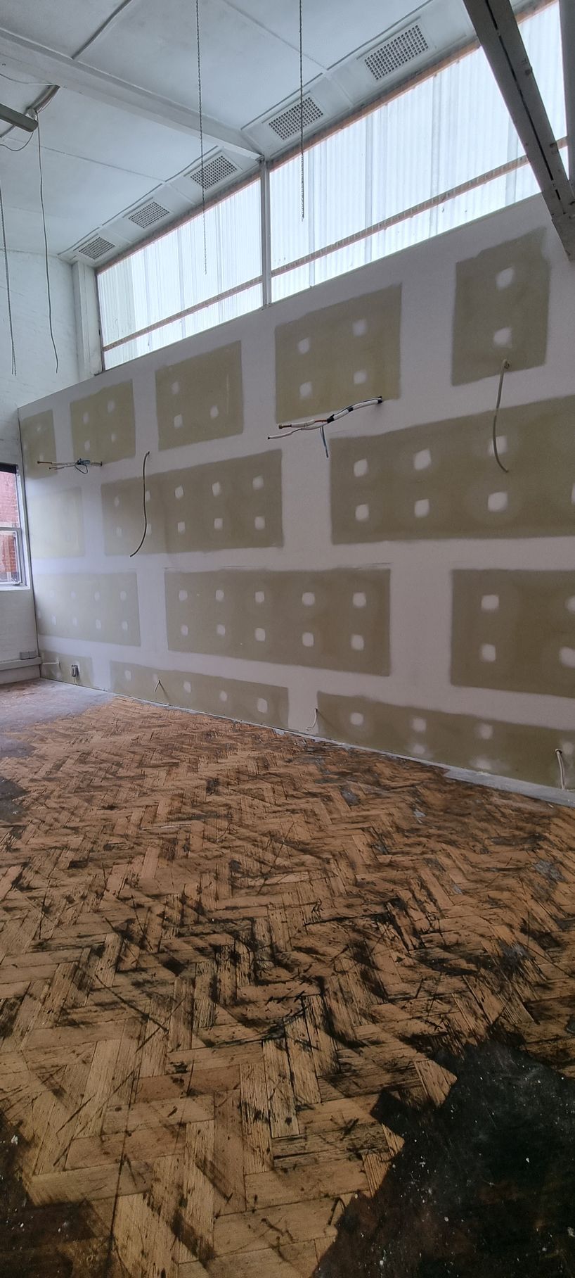 A hand uses a metal putty knife to apply white spackle or filler to a smooth white wall.