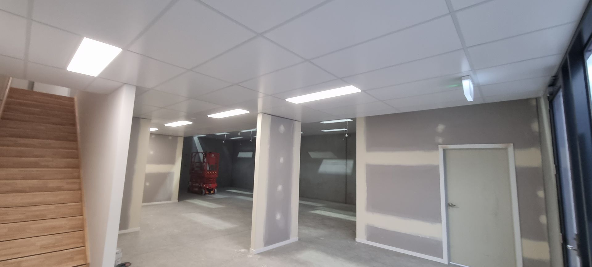 Construction site showing a circular metal stud wall frame with a curved ceiling track and an orange scissor lift.
