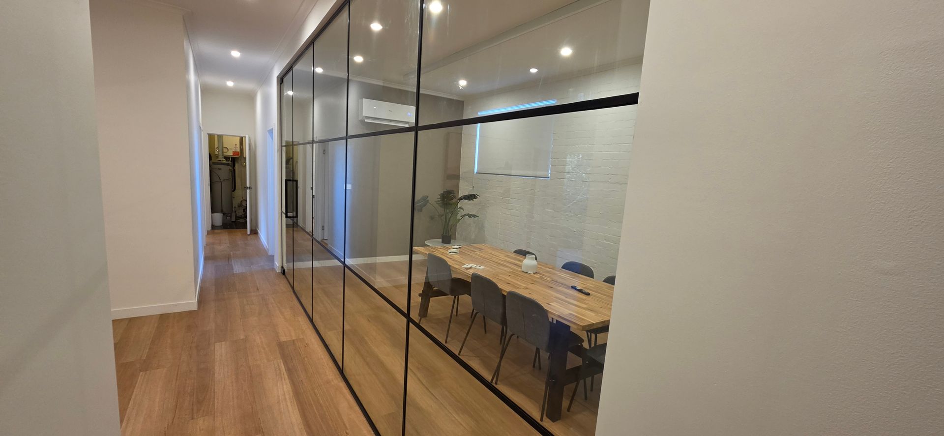 Modern office with desks, computer workstations, and glass partition walls over a herringbone wood floor.