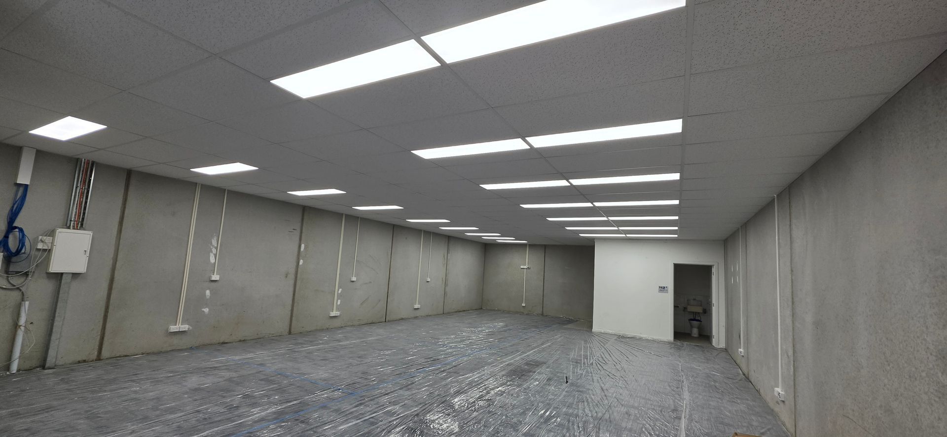 A metal grid frame for a suspended ceiling installed below a concrete ceiling with exposed wiring in a room. A metal grid frame for a suspended ceiling installed below a concrete ceiling with exposed wiring in a room.