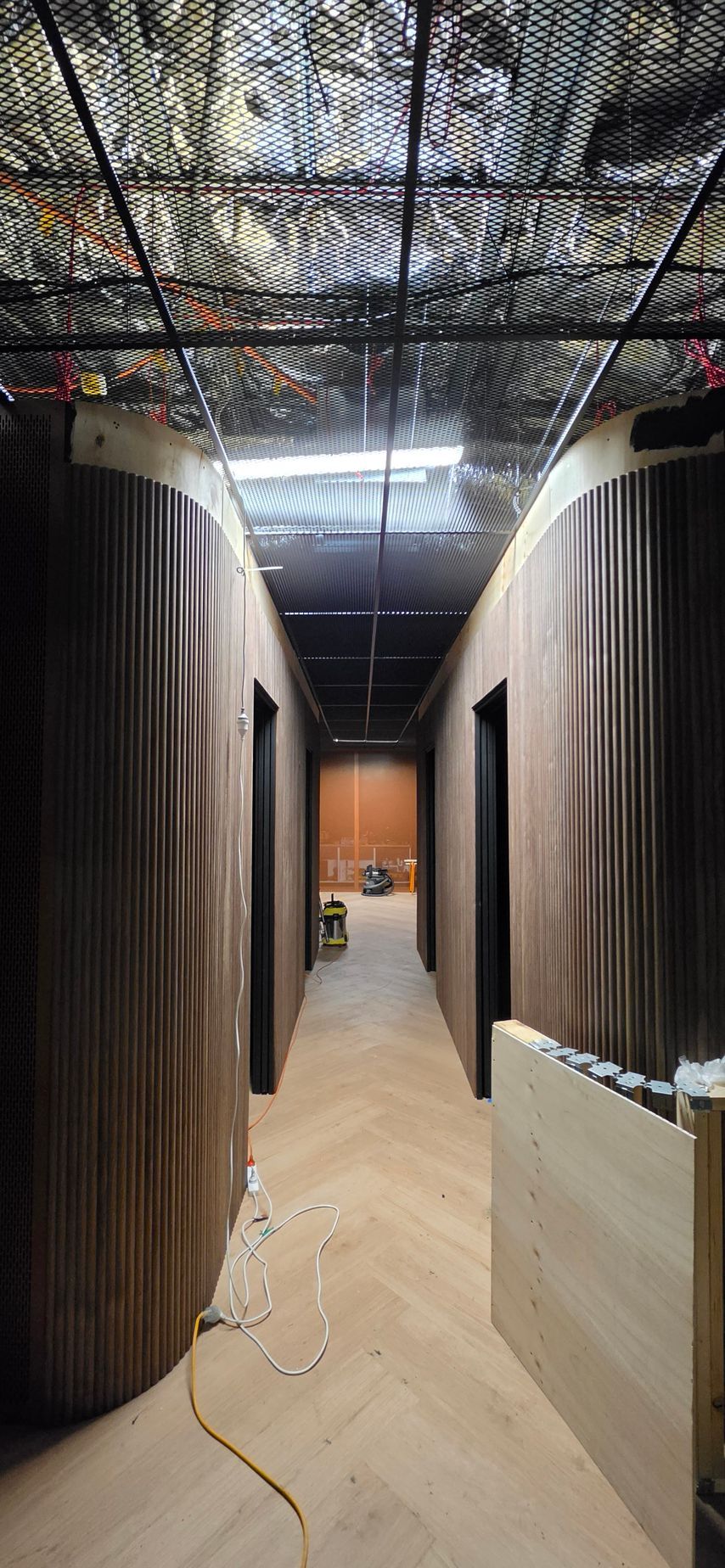 A bright dressing room area with three curtained stalls, light-colored wooden benches, and light wood wall slats.
