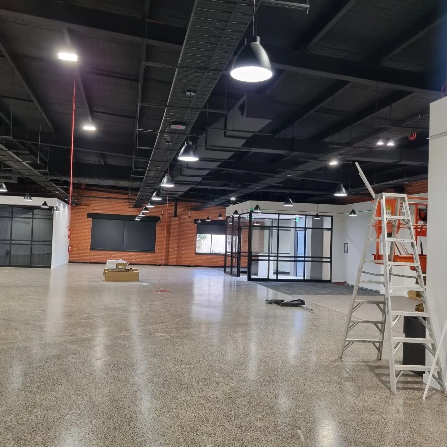 Spacious, modern office interior with an open floor plan, polished concrete floors, black ceiling, and a stepladder.
