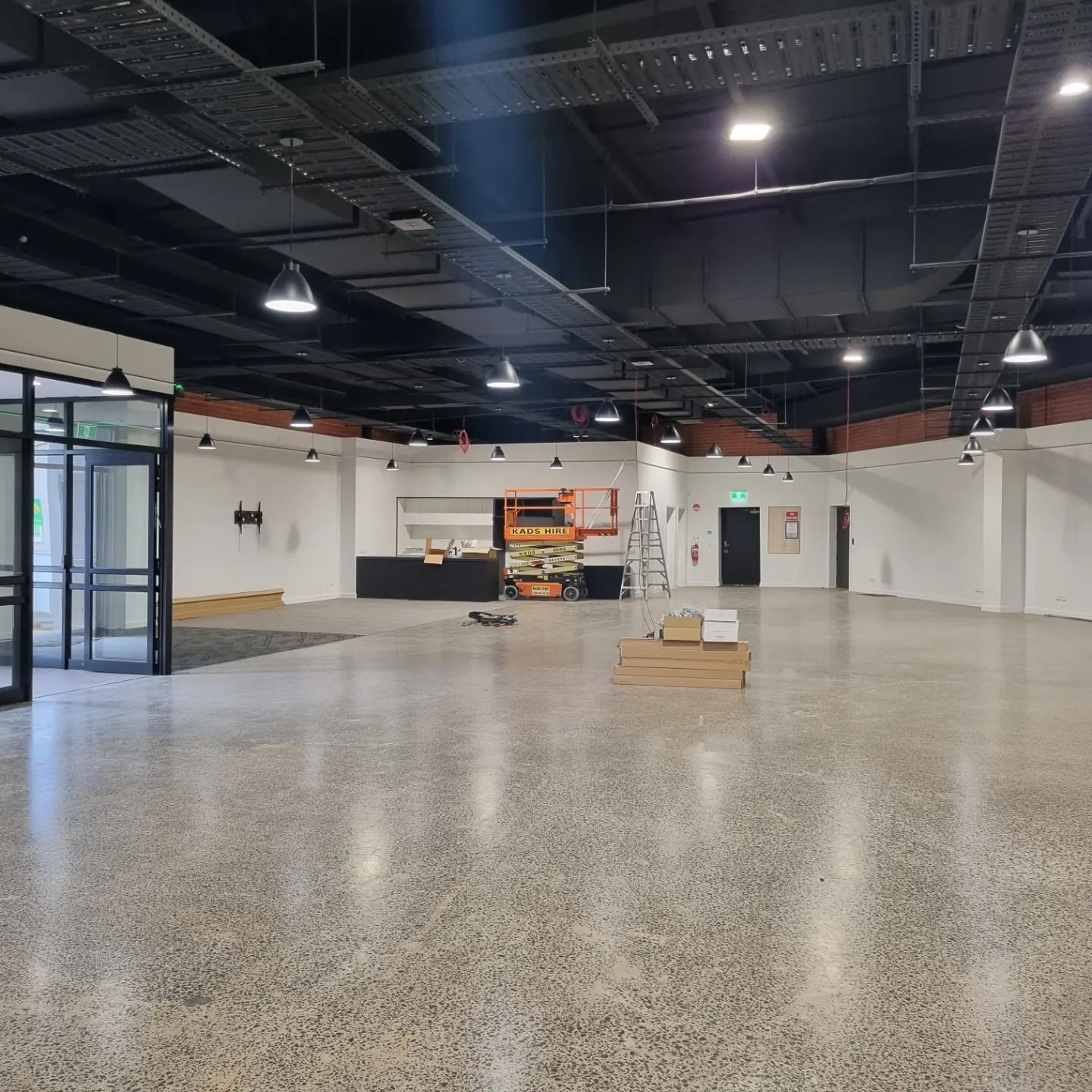An empty, industrial-style room with white walls, polished concrete floors, and exposed dark ceilings with pendant lights. An empty, industrial-style room with white walls, polished concrete floors, and exposed dark ceilings with pendant lights.