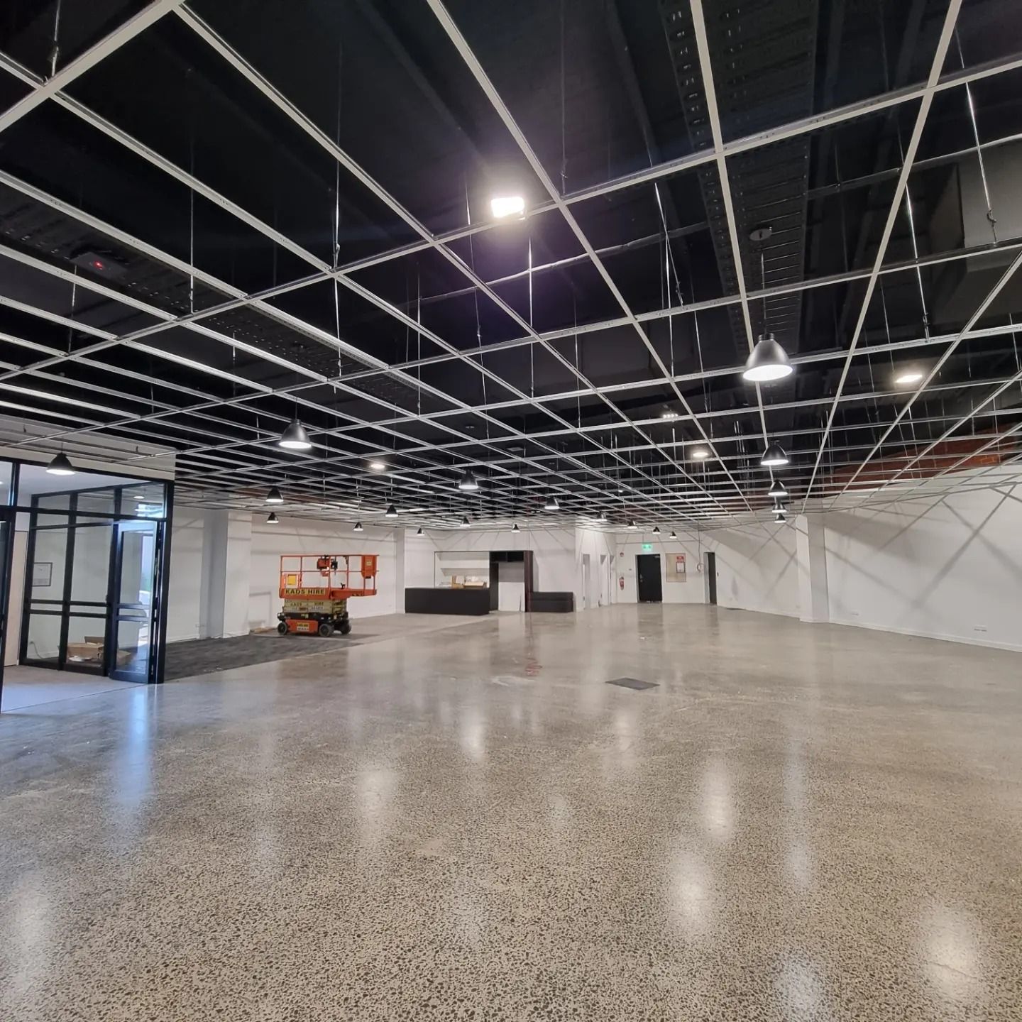 A large, empty modern commercial space with a polished concrete floor, black exposed ceiling grid, and recessed lights.