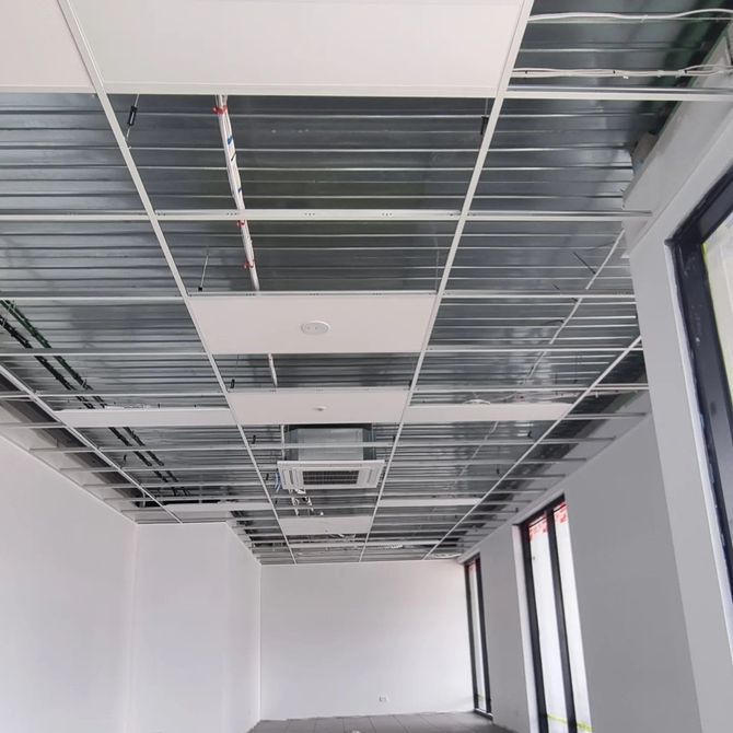 An interior view of a room under construction, showing a suspended metal grid ceiling with partially installed tiles.