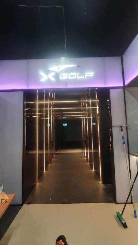 Entrance to an X-GOLF venue with a glowing sign above a dark hallway illuminated by thin vertical LED light strips. Entrance to an X-GOLF venue with a glowing sign above a dark hallway illuminated by thin vertical LED light strips.