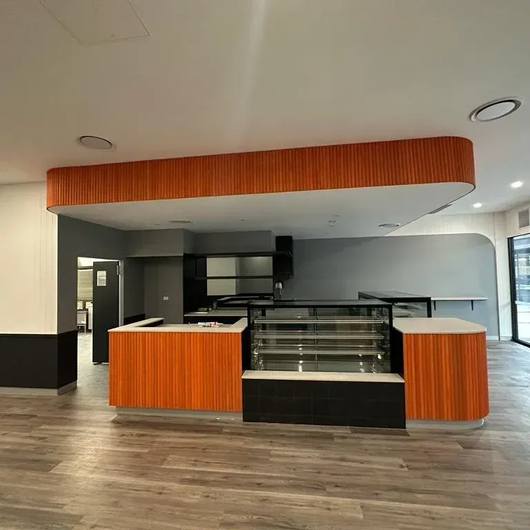 A modern, empty cafe interior featuring a counter with wood-paneling, a glass display case, and gray walls.