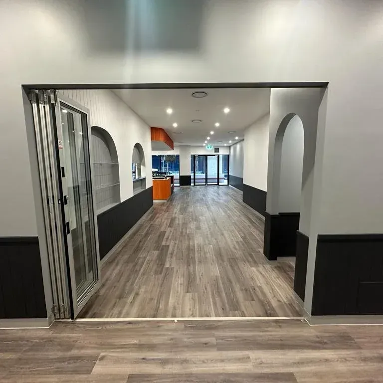 A wide, empty commercial space with light wood floors, grey walls, dark baseboards, and arched decorative wall cutouts. A wide, empty commercial space with light wood floors, grey walls, dark baseboards, and arched decorative wall cutouts.
