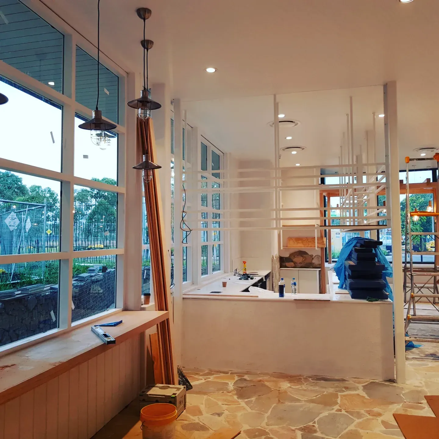 An interior view of a bright, modern commercial space under construction with floor-to-ceiling windows and stone floors. An interior view of a bright, modern commercial space under construction with floor-to-ceiling windows and stone floors.