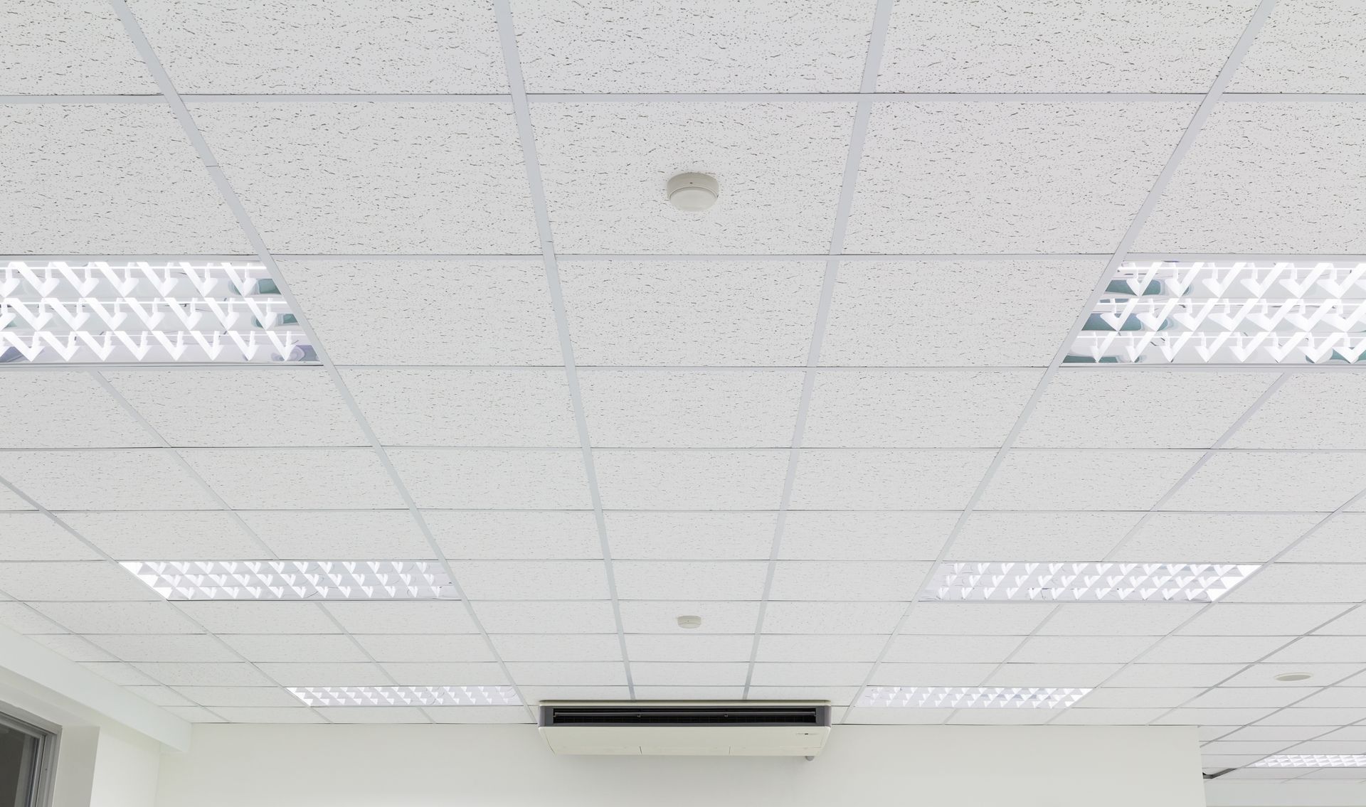 A drop ceiling in an office space with recessed fluorescent lighting fixtures and a central air conditioning vent.