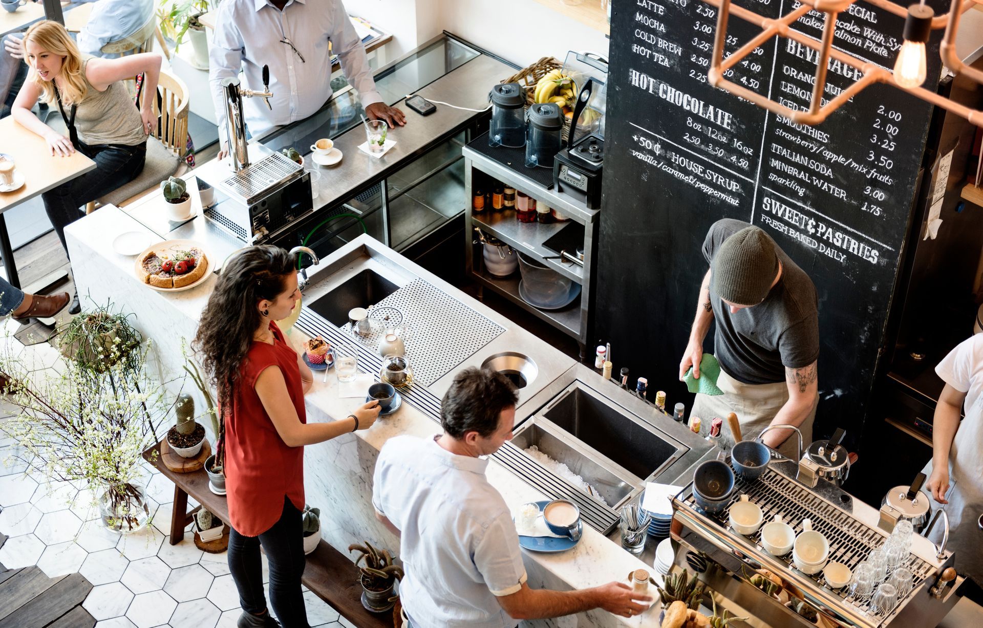 High-angle view of a busy coffee shop with staff preparing drinks and customers waiting at the counter. High-angle view of a busy coffee shop with staff preparing drinks and customers waiting at the counter.