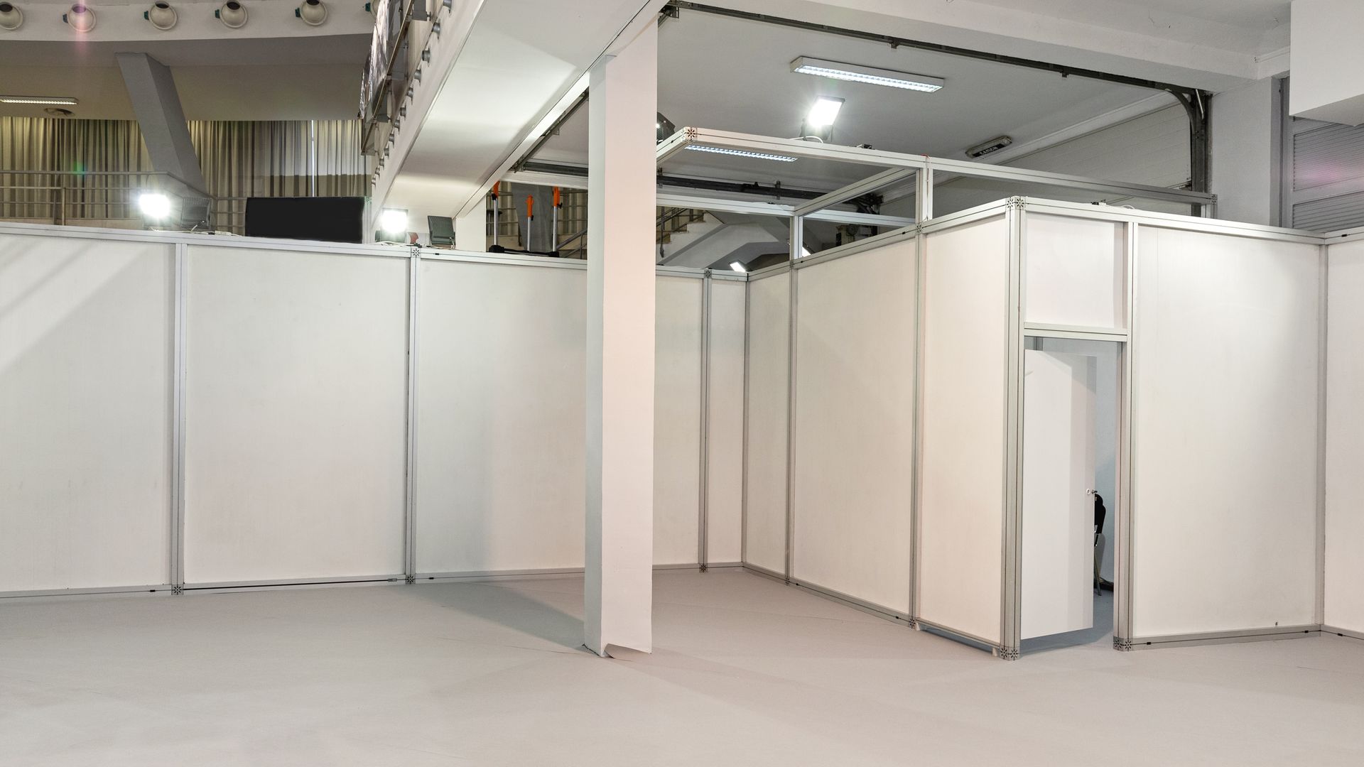 An indoor trade show booth with white modular walls, a metal frame, and a central doorway under ceiling lighting.