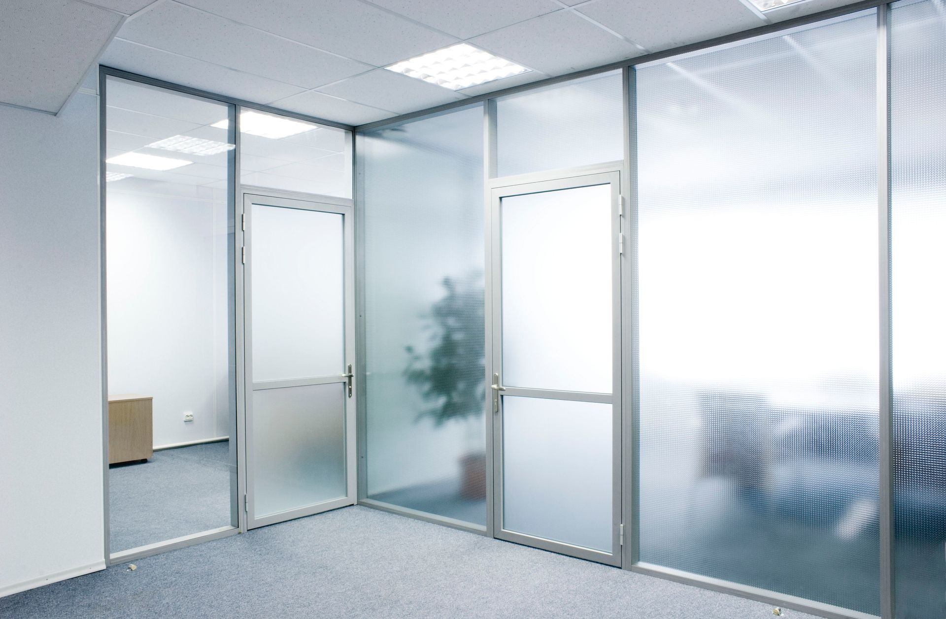 Modern office interior featuring glass partitions and doors, with frosted and ribbed glass panels separating workspace. Modern office interior featuring glass partitions and doors, with frosted and ribbed glass panels separating workspace.
