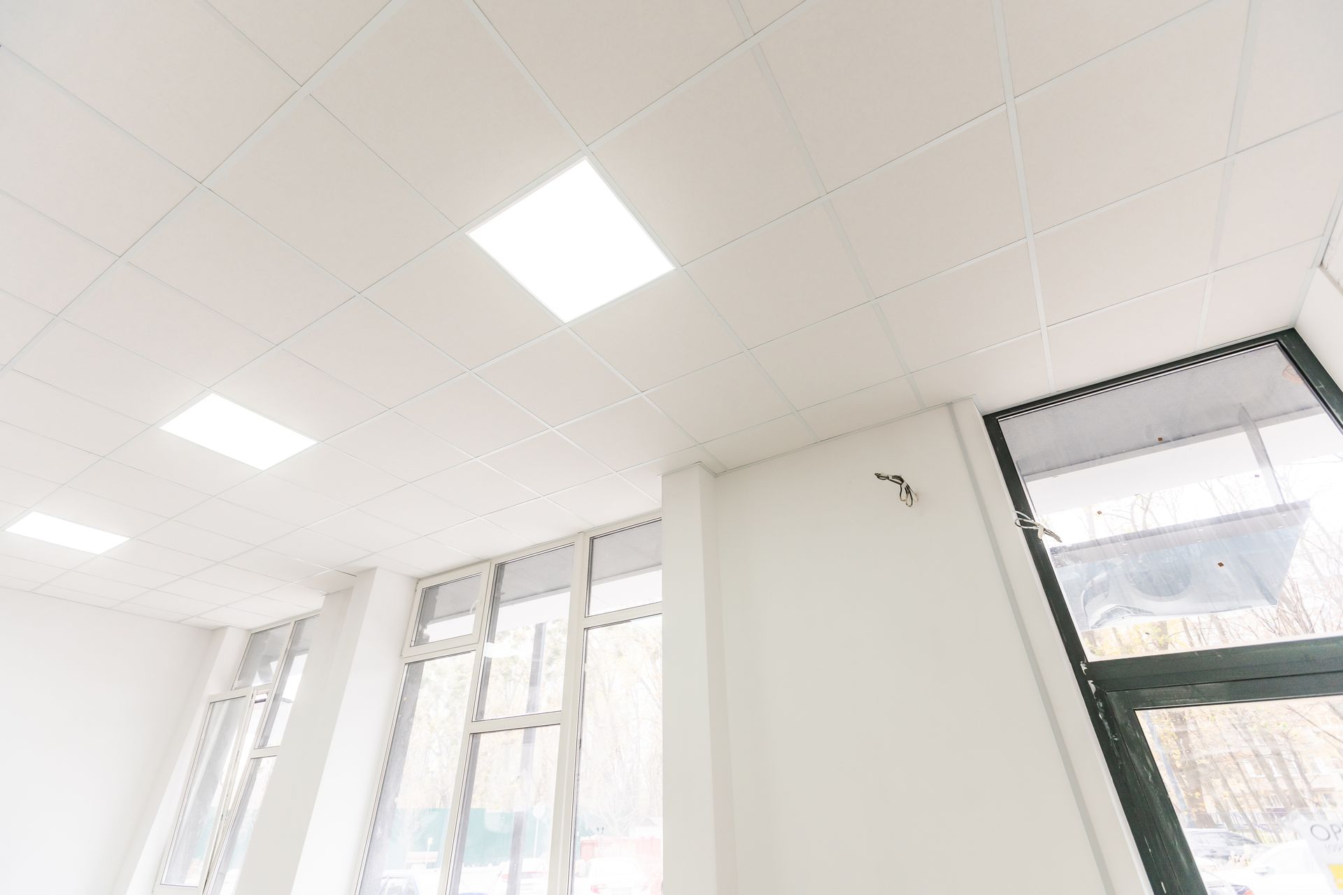 A white, drop-ceiling interior with recessed LED panel lights and tall windows along a wall.
