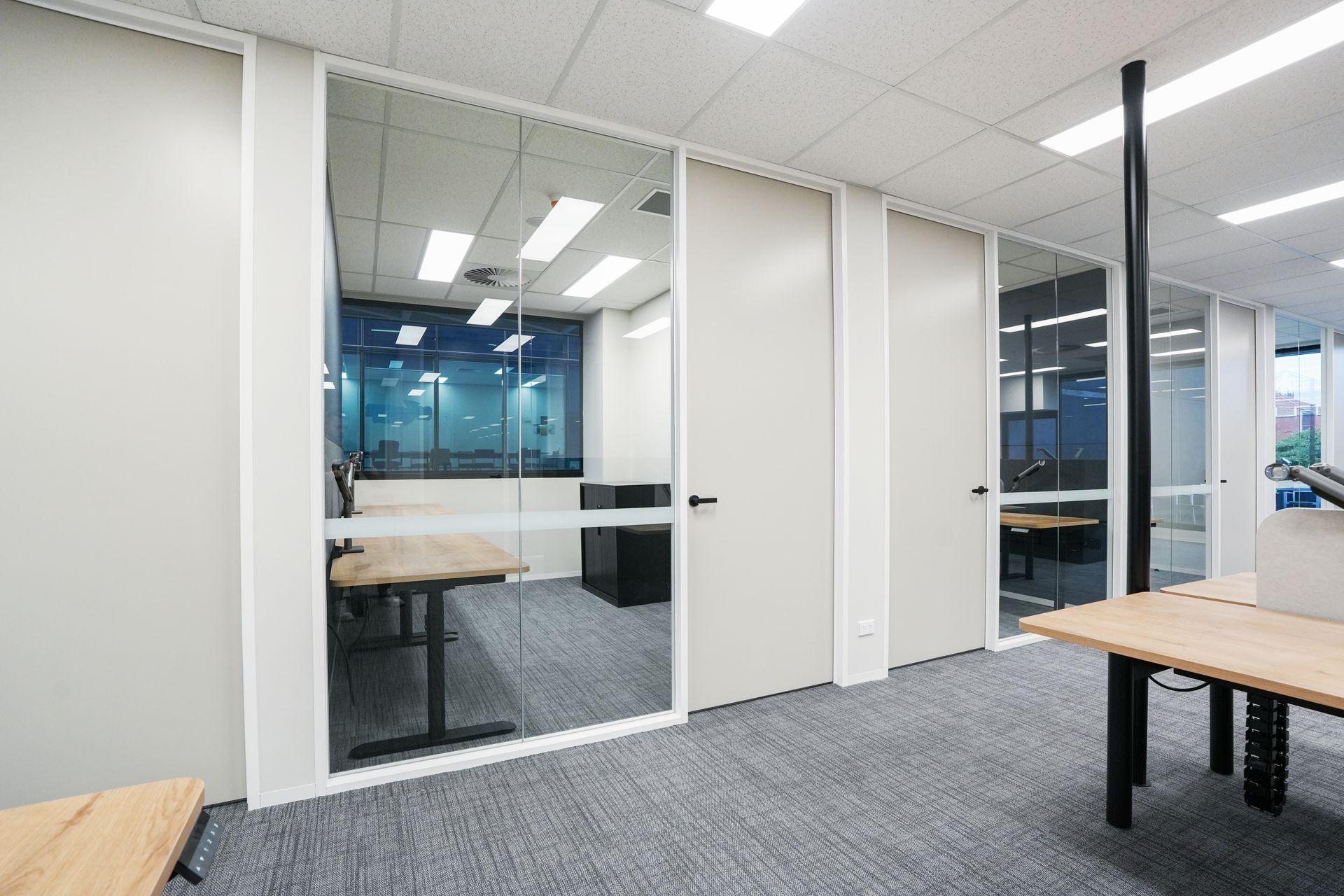 An indoor trade show booth with white modular walls, a metal frame, and a central doorway under ceiling lighting.