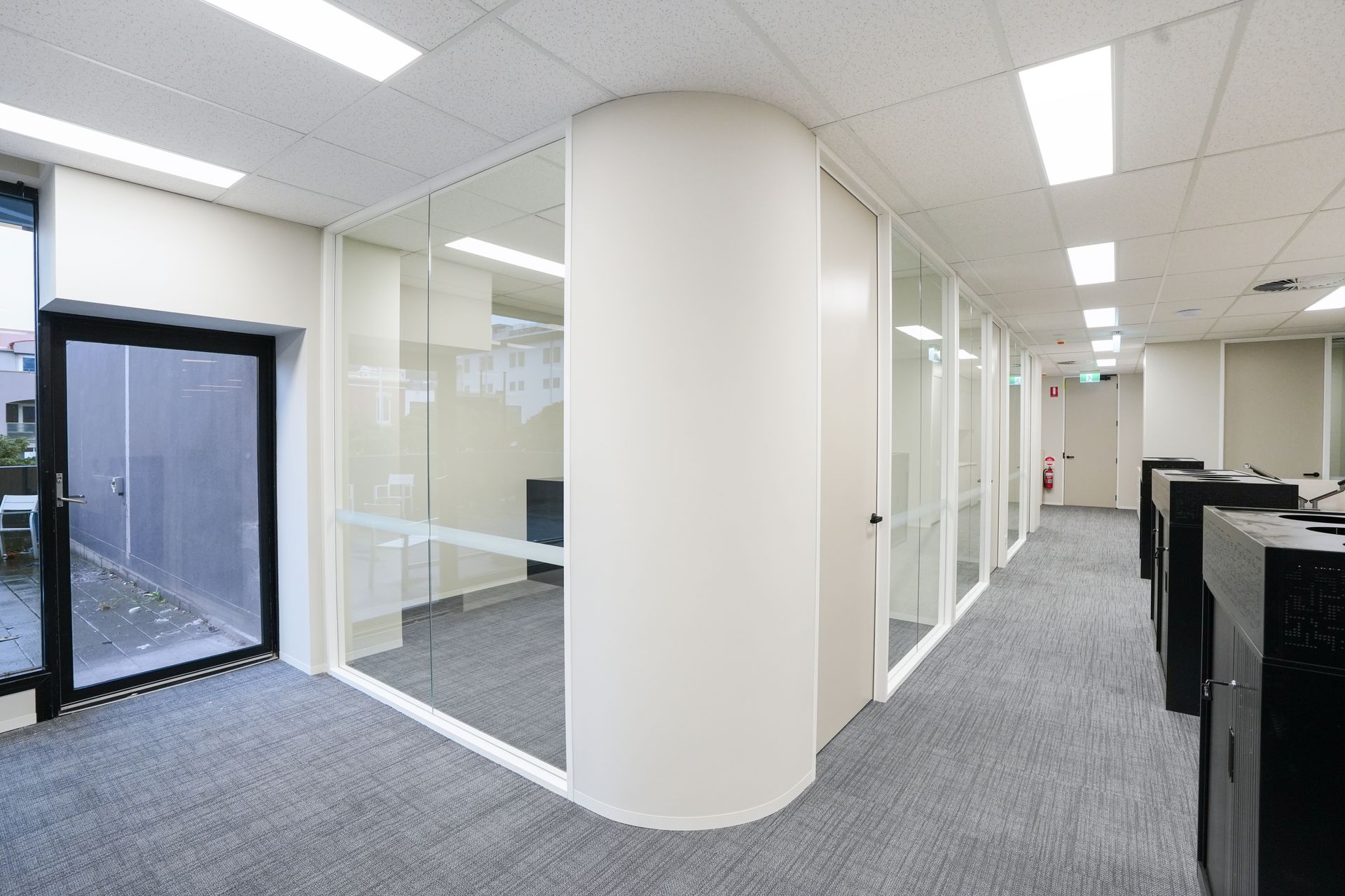Four people collaborate in a modern, light-filled office with glass walls and white brick, engaged in a group discussion.