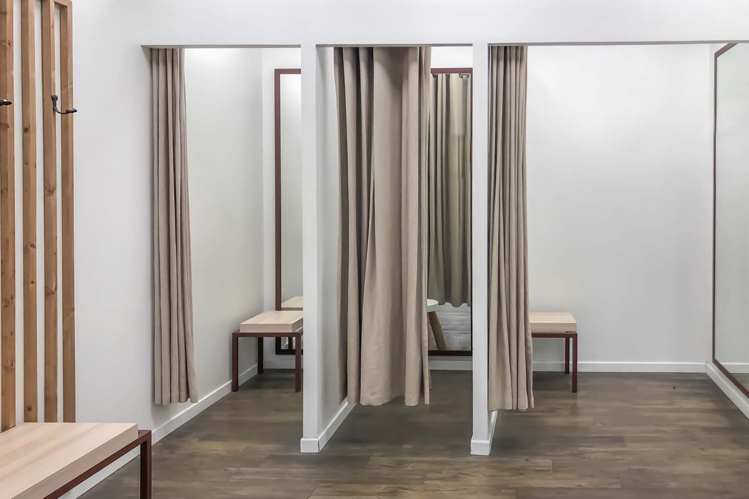 A bright dressing room area with three curtained stalls, light-colored wooden benches, and light wood wall slats. A bright dressing room area with three curtained stalls, light-colored wooden benches, and light wood wall slats.