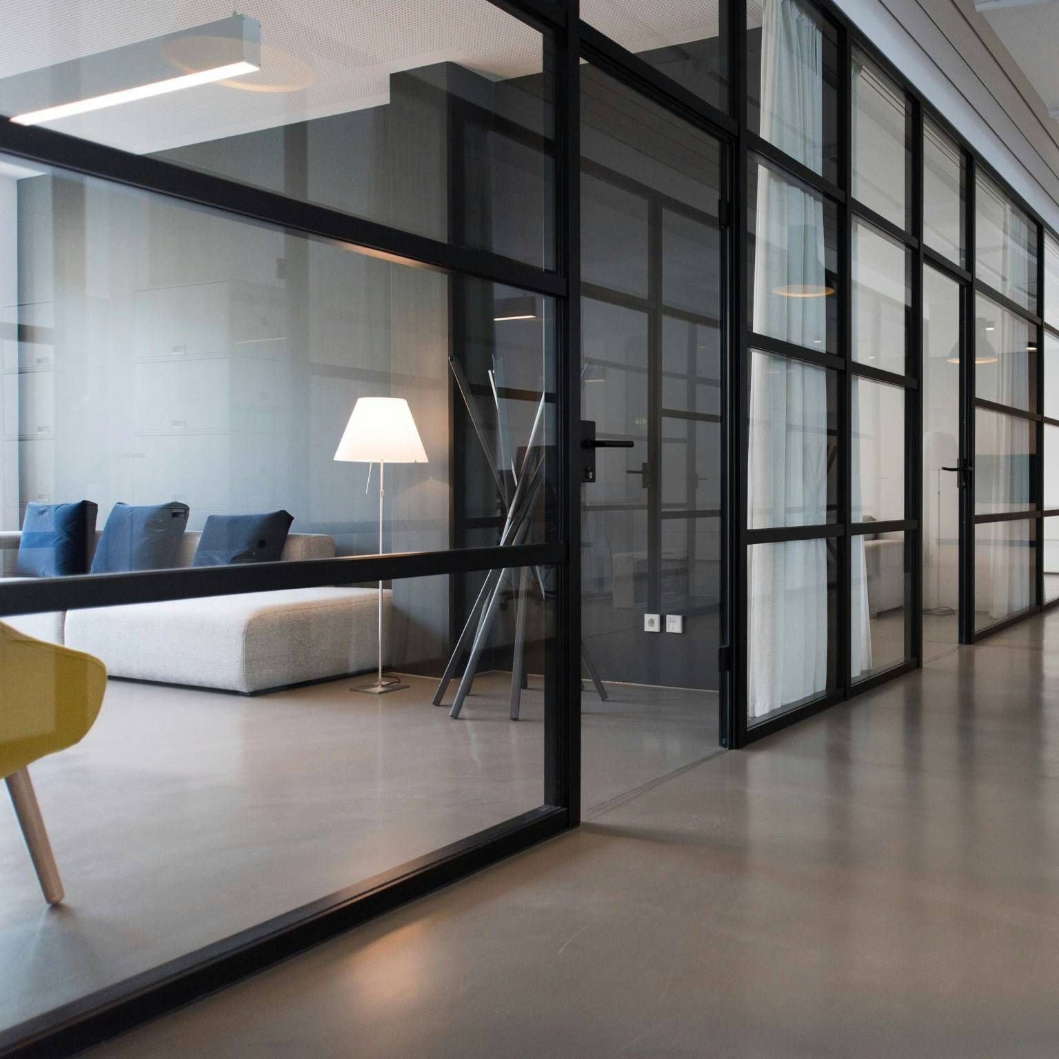 Modern office interior with glass-walled meeting rooms, minimalist furniture, and a bright, minimalist lounge area.