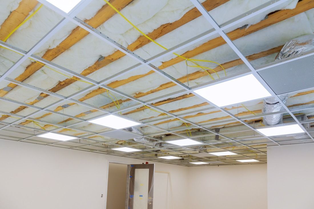 An unfinished drop ceiling with exposed insulation, metal support grids, and several installed square LED panel lights.