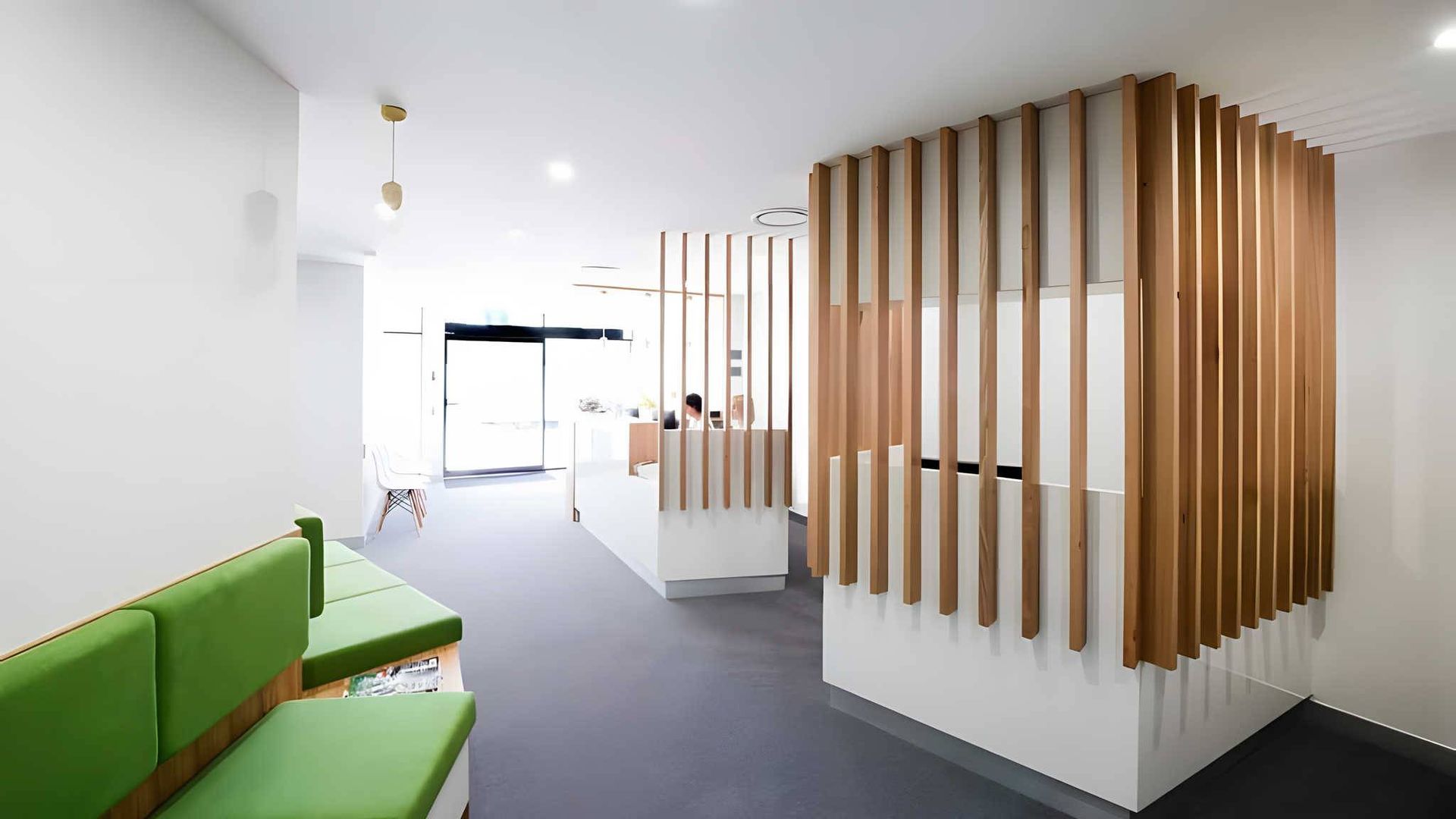 A modern waiting area with green bench seating, grey flooring, and a reception desk accented by vertical wood slats. A modern waiting area with green bench seating, grey flooring, and a reception desk accented by vertical wood slats.