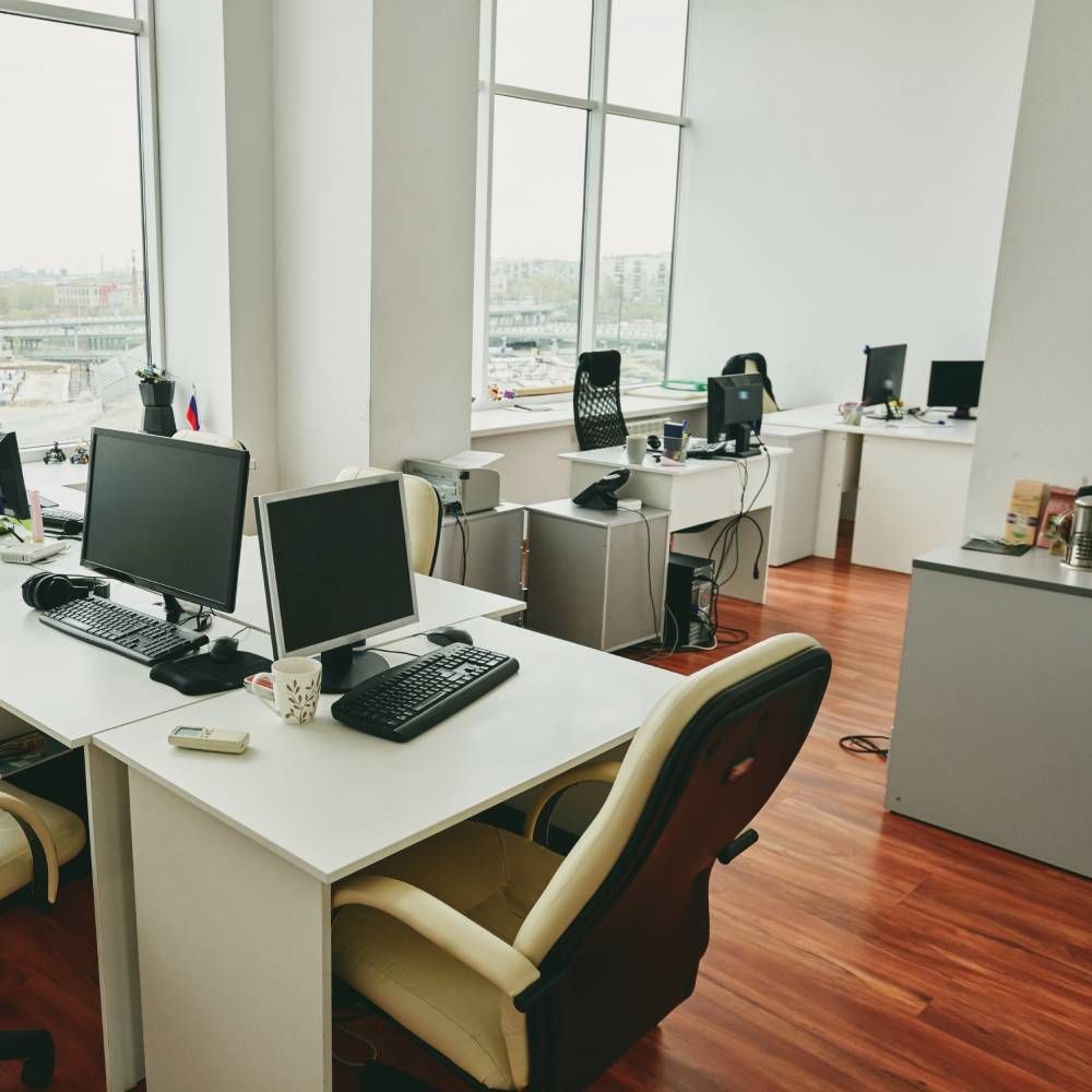 Modern office space with desks, computers, chairs, and large windows with a view of a city landscape.