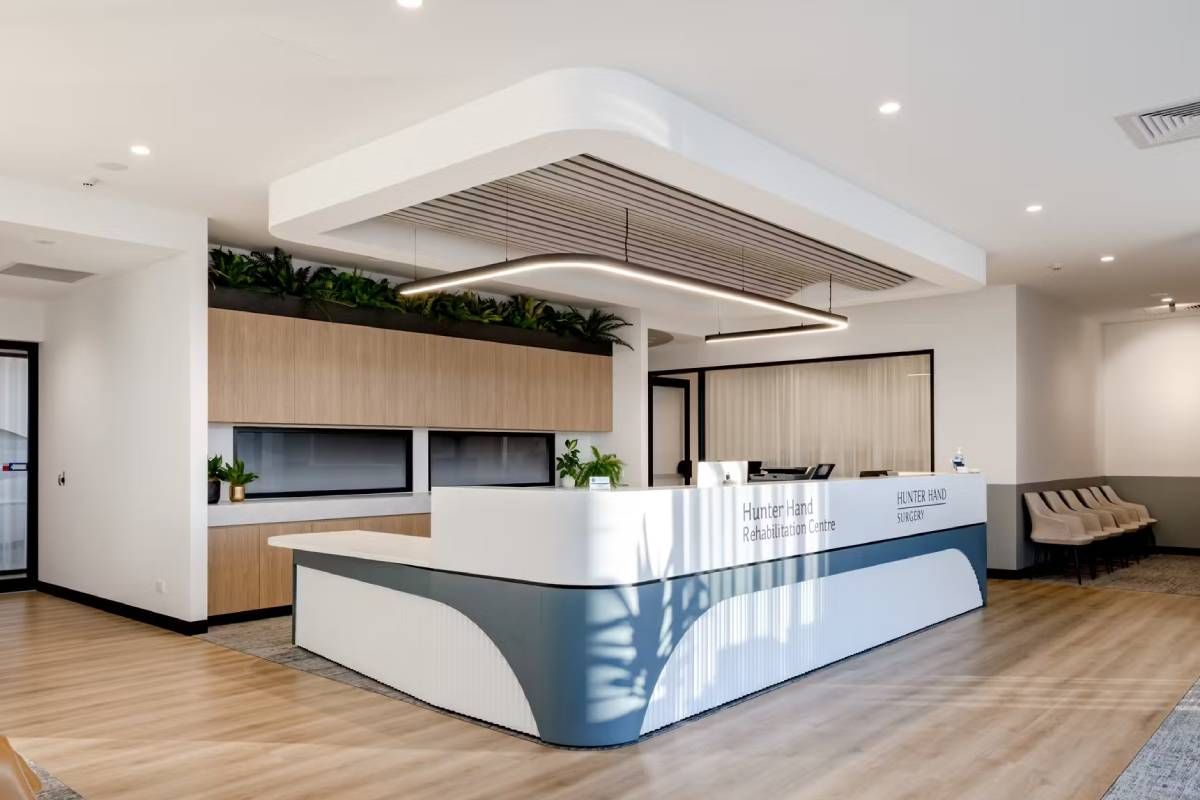 Modern reception desk in a bright office, featuring a curved blue and white counter, wood cabinets, and overhead lighting. Modern reception desk in a bright office, featuring a curved blue and white counter, wood cabinets, and overhead lighting.