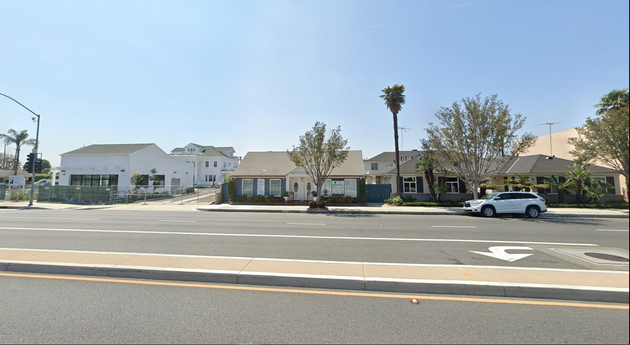 A white suv is parked on the side of the road in front of a row of houses.