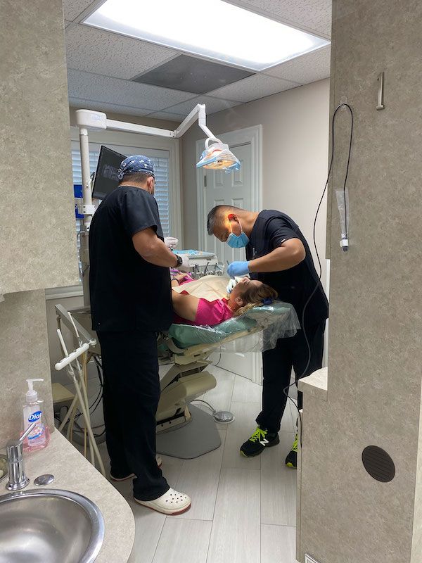 Two dentists are working on a patient in a dental office.