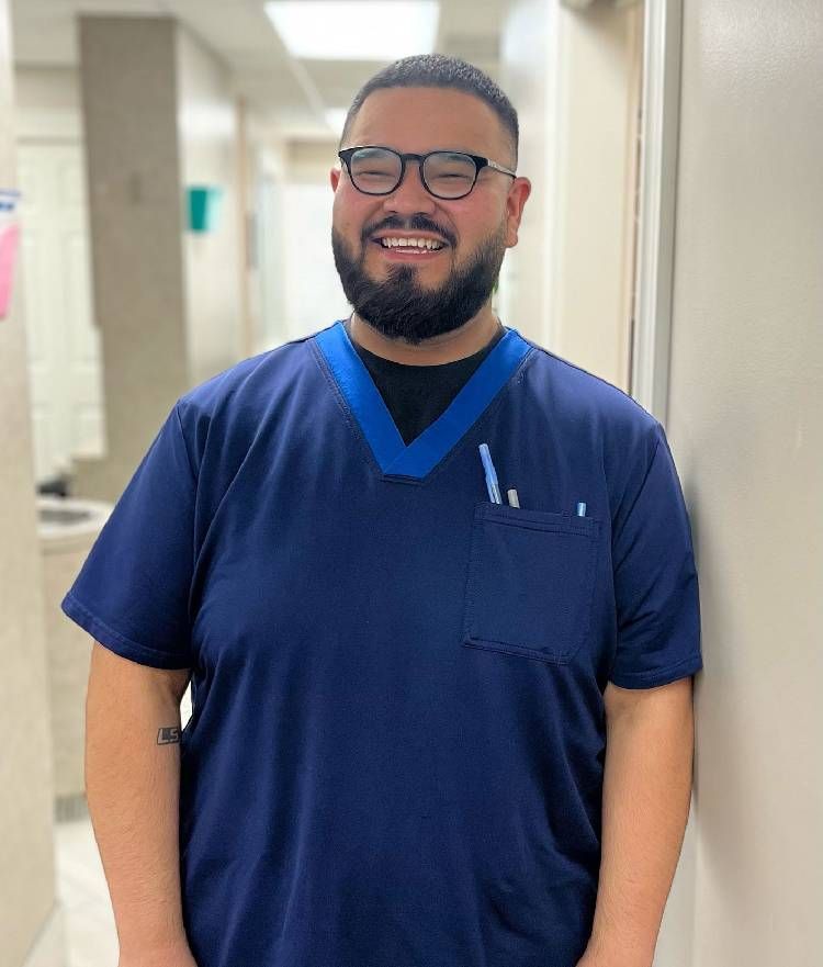 A man with a beard and glasses is wearing a blue scrub top.