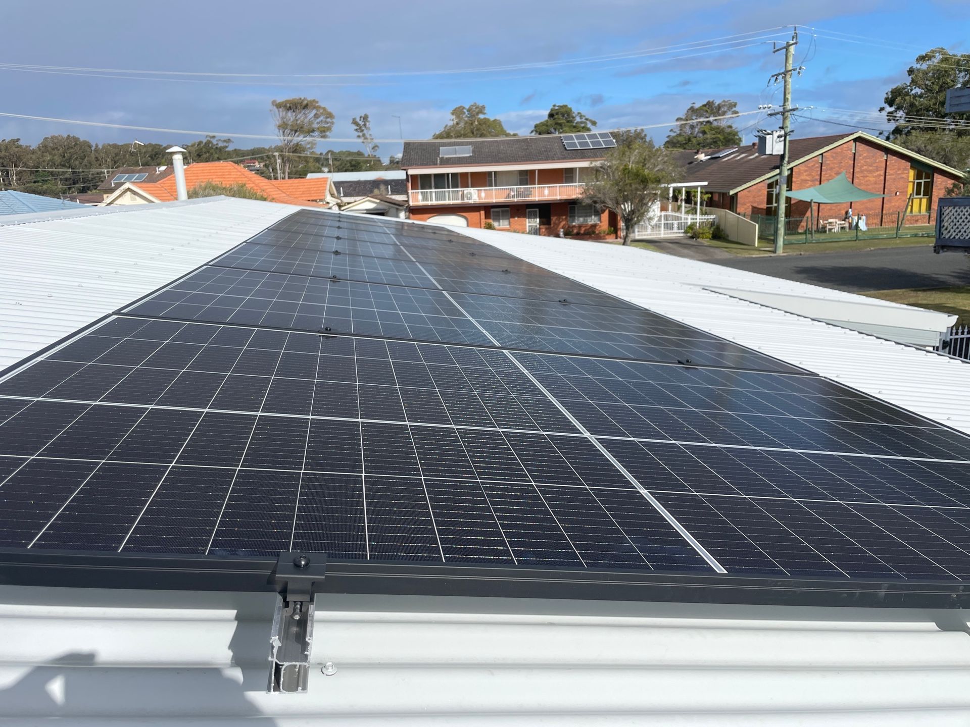 A Tesla Battery Is Mounted On A White Wall Next To A Solar Panel — Forster Solar and Lighting In Forster, NSW