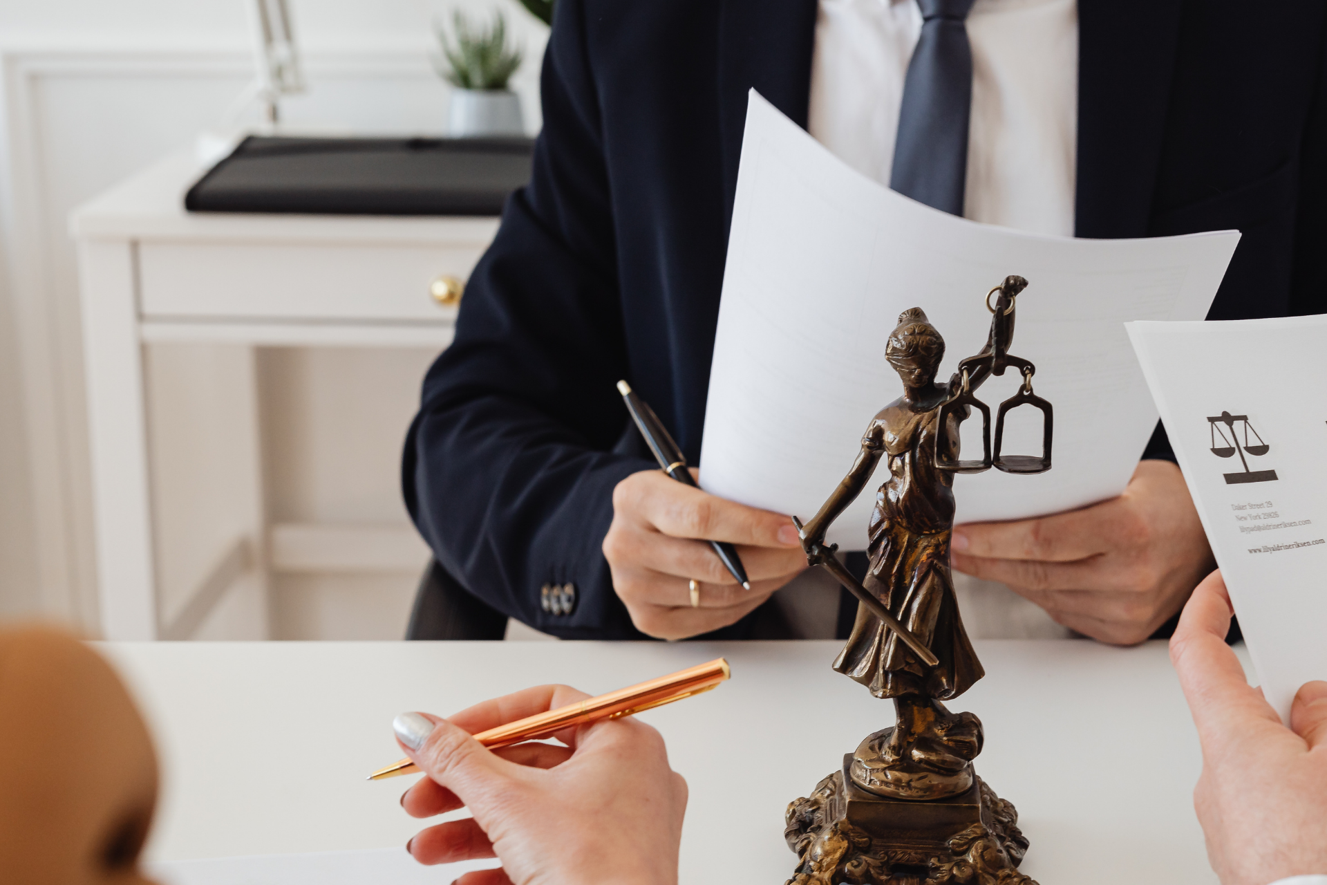 Lawyer writing notes at a desk with brass scales of justice in the foreground