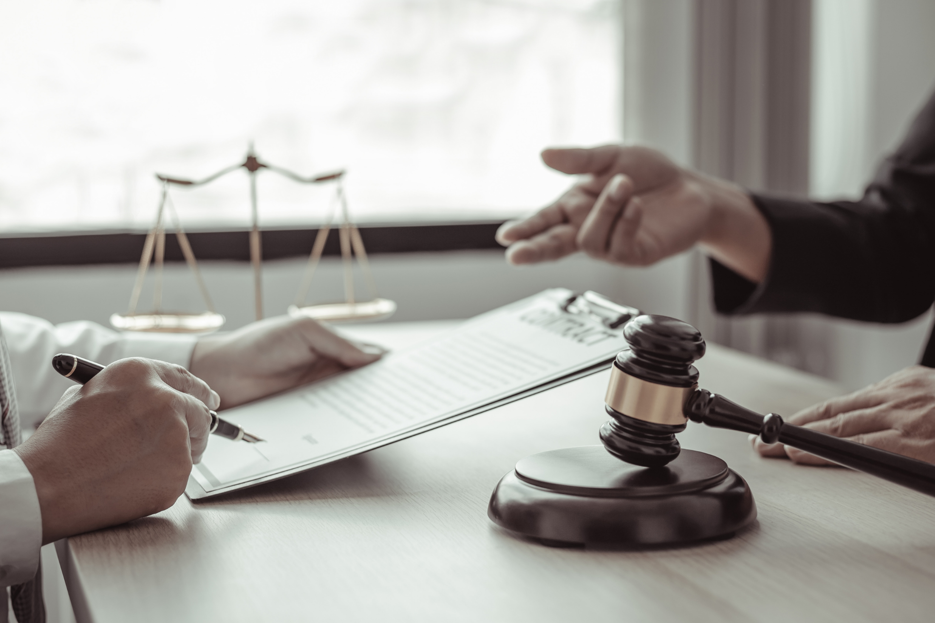 Handshake over a clipboard in a law office, with a brass justice scale on the desk.
