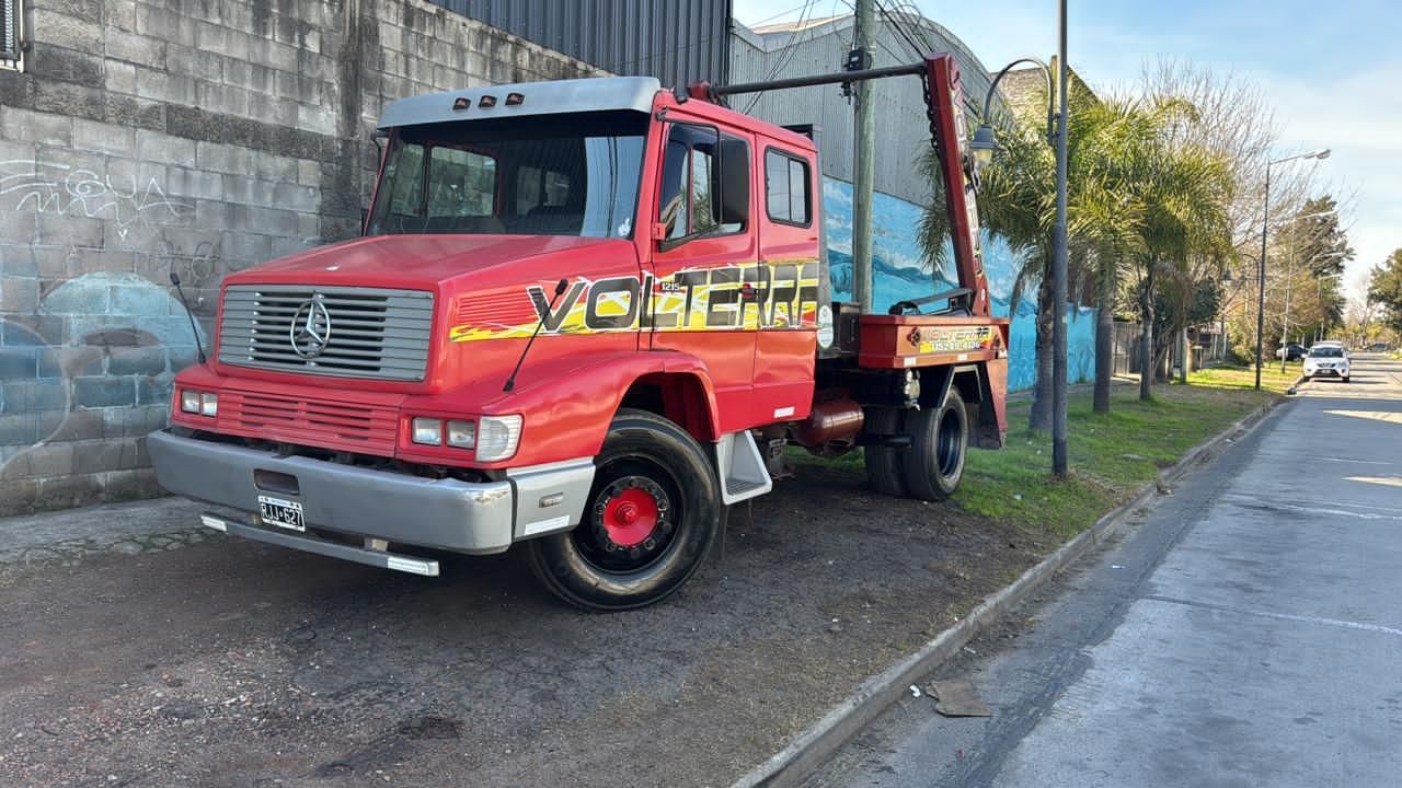 Camión volquete rojo estacionado junto a la carretera, al lado de un muro de hormigón y unos árboles