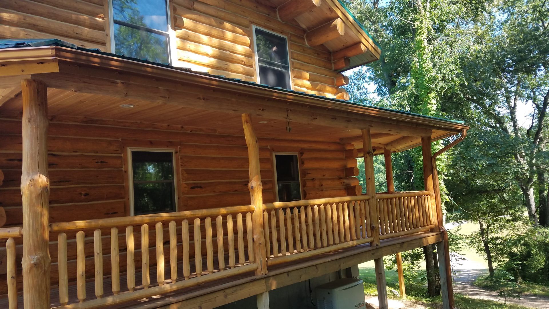 A log cabin with a large porch and railing surrounded by trees.