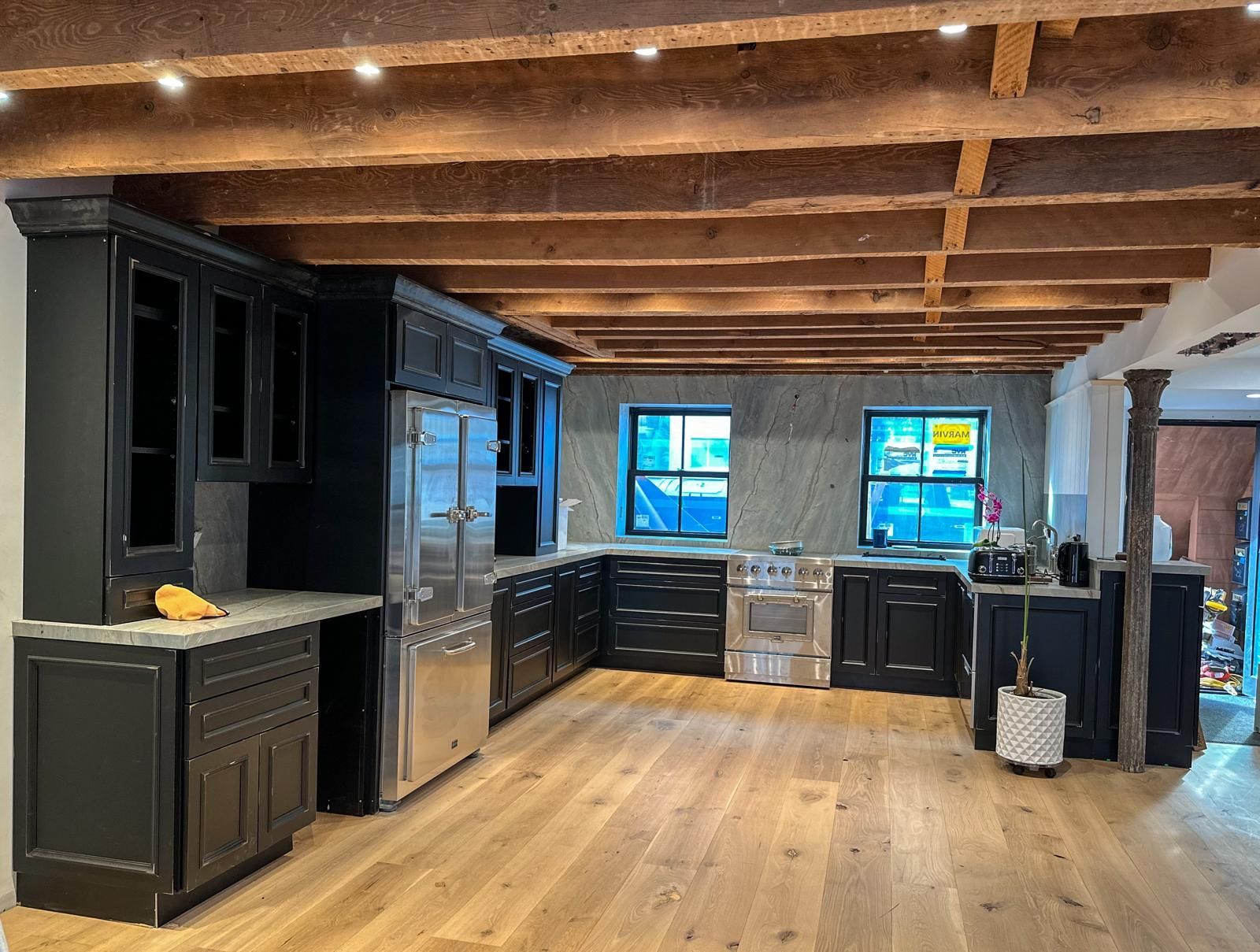 Black kitchen cabinets with stainless steel appliances, exposed wooden beams, and wood flooring.